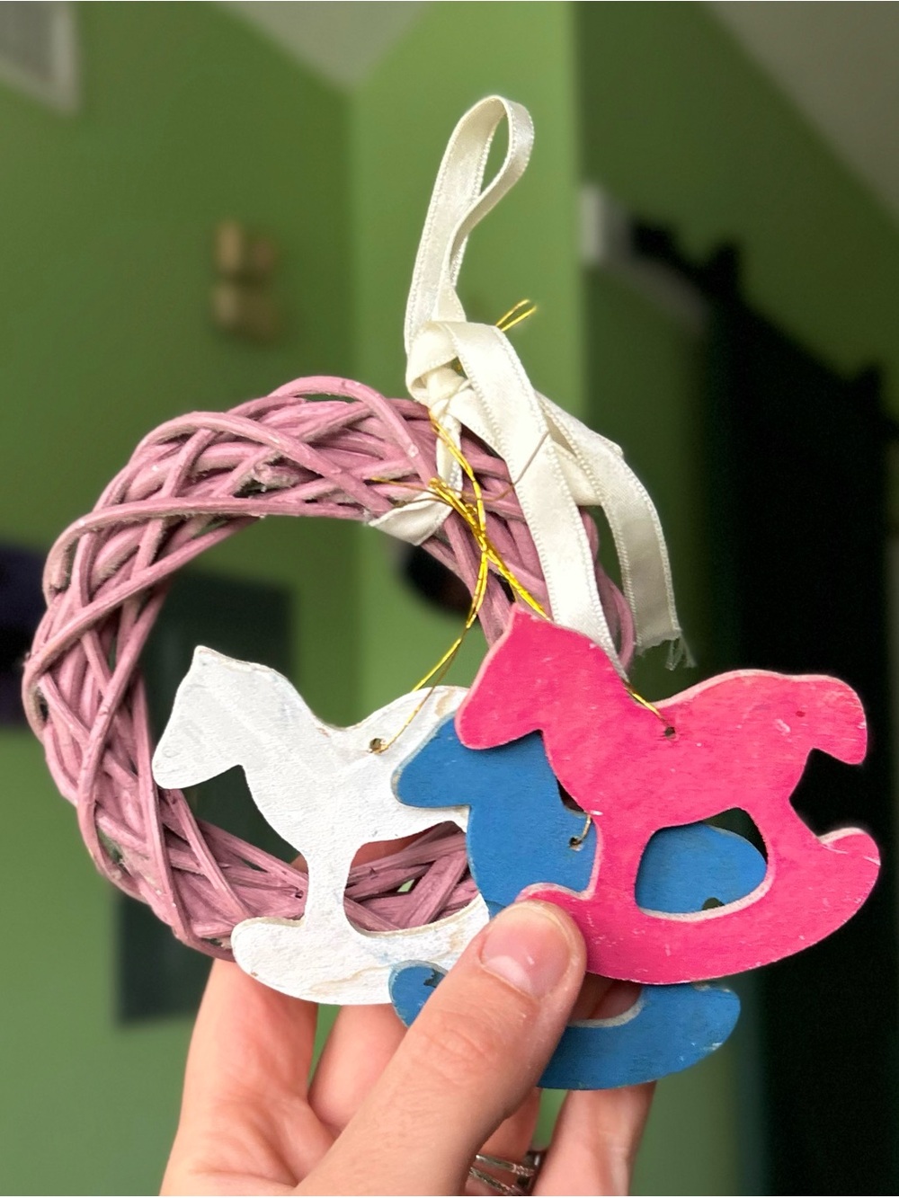 Pink, white, and blue wooden rocking horse with a pink wicker wreath